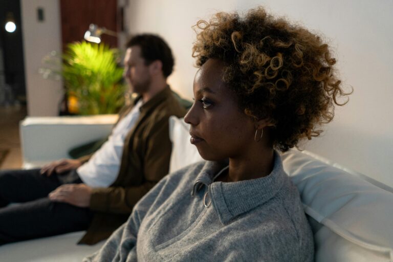 Black woman with natural curly hair sitting in the foreground looking away with a man blurred in the background